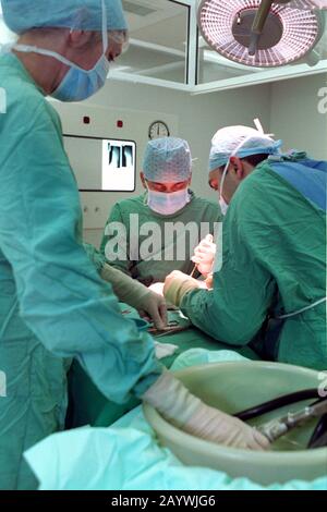 Zwei Chirurgen in einem Krankenhaus-Theater und die Scheuerschwester, die chirurgische Instrumente passieren Stockfoto