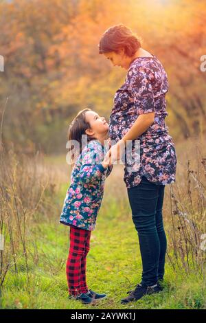 Glückliche Familie. Schwangere Mutter und kleine Tochter umarmen und küssen bei Sonnenuntergang im Herbst im Wald. Gelächter, Glück und Spaß zusammen Stockfoto