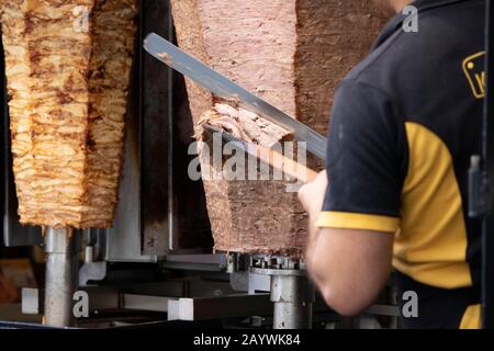 Zubereitung von Döner-Kebab-Lebensmitteln aus nächster Nähe. Beim Schneiden des Fleisches auf der Maschine wurde ein Koch fotografiert. Stockfoto