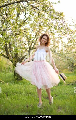 Junge attraktive Frau mit lockigem Haar wandern in einer grünen blühenden Garten. Feder romantische Stimmung. Stockfoto