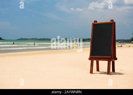 Schwarze Tafel aus leerem Holz steht im Sand am tropischen Strand Stockfoto