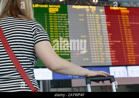 Frau schaut auf die Anzeigetafel am Flughafen. Wählen Sie ein Land für Reisen oder Migration aus. Stockfoto