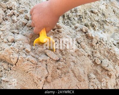 Hand des Kindes, das im Sandkasten mit gelber Schaufel spielt. Stockfoto