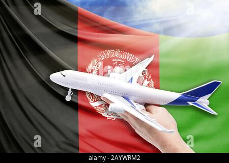 Flugzeug in der Hand mit Nationalflaggen Afghanistans auf blauem Himmel mit Sonnenstrahlen Stockfoto