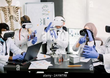 Wissenschaftler Ärzte in Mänteln, Handschuhe und tragen eine virtuelle Realitätsbrille, die im Labor arbeitet und medizinische Forschung macht. Biotechnologie, Chemie, Wissenschaft Stockfoto