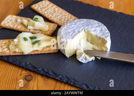 Camembert-Käse und Ganzweizenkracker auf schwarzem Schieferkäseplatt Stockfoto