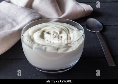 Schüssel mit natürlichem griechischen Joghurt mit Löffel und Serviette auf Schwarzer rustikaler Hintergrund - cremig weißer Joghurt Stockfoto