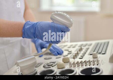 Der Arzt, der an einem Ultraschallscanner arbeitet, mit einer Hand am Joystick und mit der anderen Hand, der einen Sensor im Fenster hält. Stockfoto