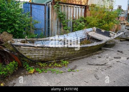 Klinker baute Lachsfischboot namens Ulla fast verrottet und legte in einem Hof neben einigen Lagerbehältern. Stockfoto