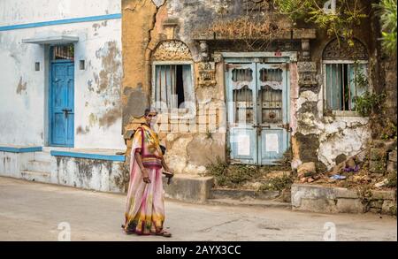 Eine alte Indianerin, die eine bunte Saree trägt, spaziert an alten verfallenen Häusern auf den Straßen der Insel Diu vorbei. Stockfoto