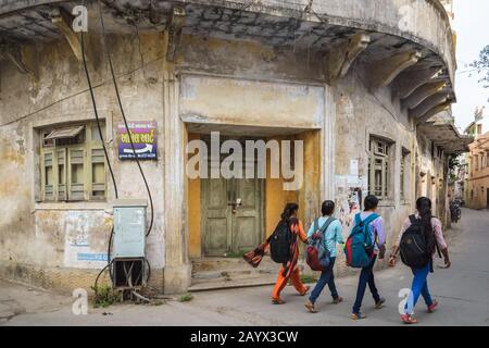 DIU, Indien - Dezember 2018: Ein altes Haus mit hübschen Fenstern, verblichener kolonialer Art-Deco-Architektur, vier Mädchen gehen auf der Straße draußen vorbei. Stockfoto