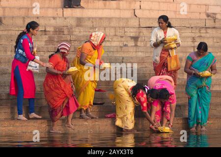 Varanasi, INDIEN, 18. JANUAR 2019: EINE Gruppe von Frauen, die bunte traditionelle Kleider tragen, betet, bevor sie bei Sonnenaufgang ein spirituelles Bad beginnen Stockfoto