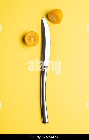 Mit Messer auf gelbem Hintergrund öffnete sich die Kumquat-Frucht. Stockfoto
