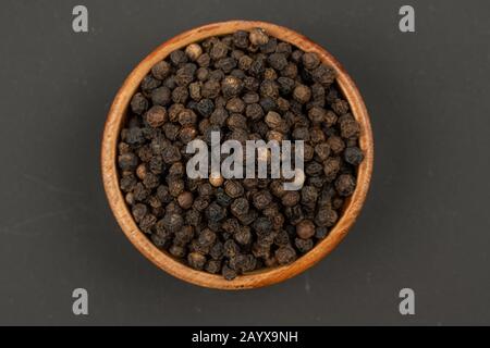 Eine kleine Holzschale mit schwarzen Pfefferkörnern auf schwarzem Grund Stockfoto