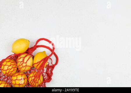 Einkaufstasche aus rotem Mesh mit gelben Zitronen auf weißem Hintergrund. Draufsicht, flaches Layout, Kopierbereich. Kein Abfall, umweltfreundliches Konzept. Stockfoto