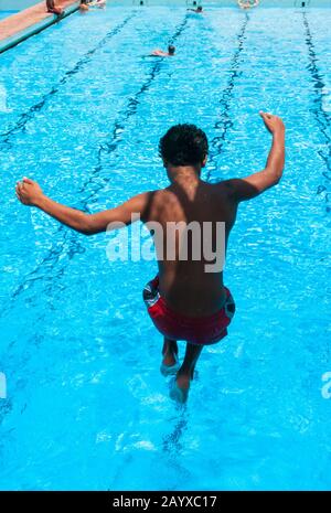 Der Junge taucht in der Luft in den Swimmingpool ein Stockfoto