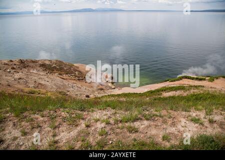 Dampf steigt am Steamboat Point am Ufer des Yellowstone Lake mit weit entfernten Bergen und Wolken im Yellowstone National Park, Wyomin, vom Boden Stockfoto