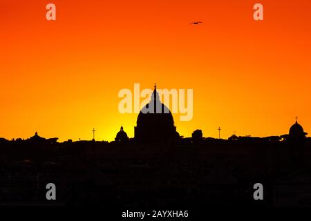 Sonnenuntergang auf der Skyline der Stadt Rom, mit der Kuppel des Petersdoms im Zentrum. Intensive gelb-orange Farbe und Horizont gegen das Licht. Stockfoto