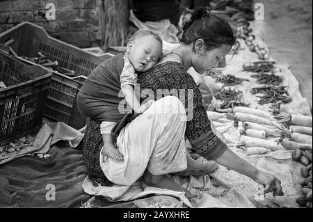 Nicht identifizierte nepalesische Frau mit einem kleinen Kind, die Gemüse in Bhaktapur verkauft, das von der UNESCO als Weltkulturerbe für ihre reiche Kultur, Tempel, gelistet ist Stockfoto