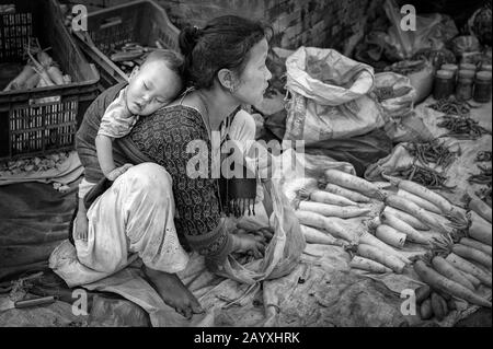 Nicht identifizierte nepalesische Frau mit einem kleinen Kind, die Gemüse in Bhaktapur verkauft, das von der UNESCO als Weltkulturerbe für ihre reiche Kultur, Tempel, gelistet ist Stockfoto