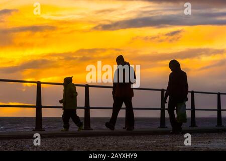 West Bay, Dorset, Großbritannien. Februar 2020. Wetter in Großbritannien. Eine Familie, die in den Halbzeitschulferien entlang der Küste entlang spazierte, setzte sich gegen einen stimmungsvollen Sonnenuntergang in der West Bay in Dorset durch. Bildnachweis: Graham Hunt/Alamy Live News Stockfoto