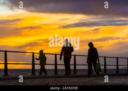 West Bay, Dorset, Großbritannien. Februar 2020. Wetter in Großbritannien. Eine Familie, die in den Halbzeitschulferien entlang der Küste entlang spazierte, setzte sich gegen einen stimmungsvollen Sonnenuntergang in der West Bay in Dorset durch. Bildnachweis: Graham Hunt/Alamy Live News Stockfoto