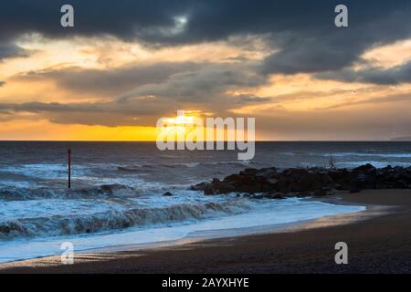 West Bay, Dorset, Großbritannien. Februar 2020. Wetter in Großbritannien. Die untergehende Sonne hinter dunklen Wolken kurz vor Sonnenuntergang an der West Bay in Dorset. Bildnachweis: Graham Hunt/Alamy Live News Stockfoto