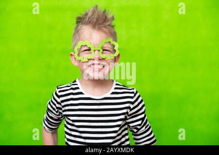 Portrait Kleiner lächelnder kaukasischer Junge in Maske aus Leprechaun Shamrock-Kleeblatten für den irischen St. Patrick's Day auf grünem Studiohintergrund. Copyspace Stockfoto