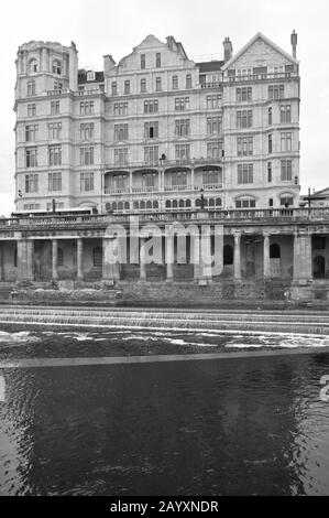 Ein Blick über den Fluss Avon mit Pulteney Wehr im Vordergrund mit dem ehemaligen Empire Hotel dahinter Stockfoto