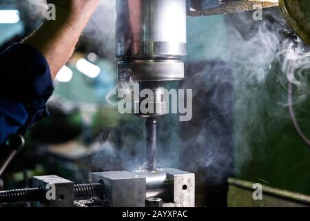 Industrielle Stahlbohrungen mit Rauchnahaufnahme mit selektivem Fokus. Manuelle Zuführung von Hand. Werkstück im Schraubstock auf Tisch. Stockfoto