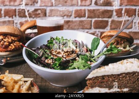 Auswahl an Gerichten, Salat mit Ziegenkäse hausgemachte Hamburger mit pommes frites, Getränk und Kuchen auf dem Holztisch. Isoliertes Bild. Stockfoto