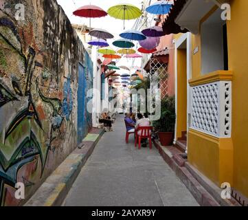 Streetart und Sonnenschirme sorgen für Farbe und Schatten auf Callejon Angosto in Gettemani, Cartagena, Kolumbien Stockfoto