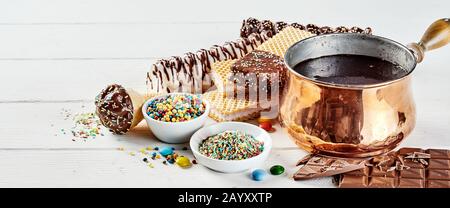 Zubereitung schokoladenbezogener leckerer Gourmet-Gebäckstücke mit geschmolzener Schokolade in einem glänzenden Kupfertopf neben Backzutaten und einer Vielzahl von Plätzchen an Stockfoto