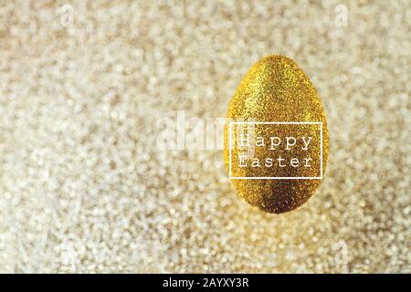 In der Luft hängt ein goldenes Ei. Auf einem strukturierten goldenen Hintergrund. Das Konzept zum Thema Ostern. Stockfoto