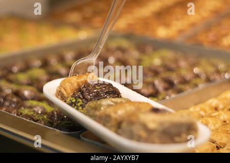 Baklavar wird in verschiedene Geschmacksrichtungen in Kunststoffplatten gegeben und hat eine Kunststoffgabel darauf. Er wurde vor den Markt gebracht. Stockfoto