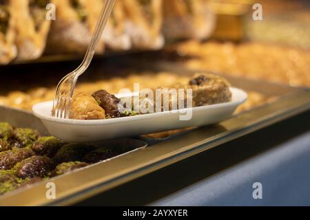 Baklavar wird in verschiedene Geschmacksrichtungen in Kunststoffplatten gegeben und hat eine Kunststoffgabel darauf. Er wurde vor den Markt gebracht. Stockfoto