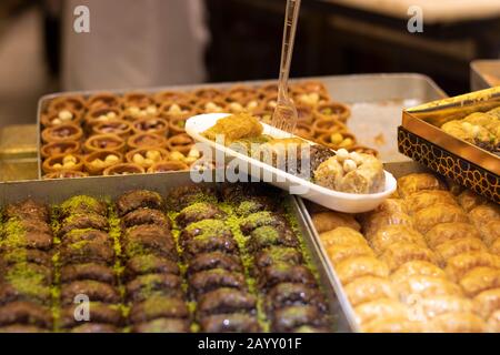 Baklavar wird in verschiedene Geschmacksrichtungen in Kunststoffplatten gegeben und hat eine Kunststoffgabel darauf. Er wurde vor den Markt gebracht. Stockfoto