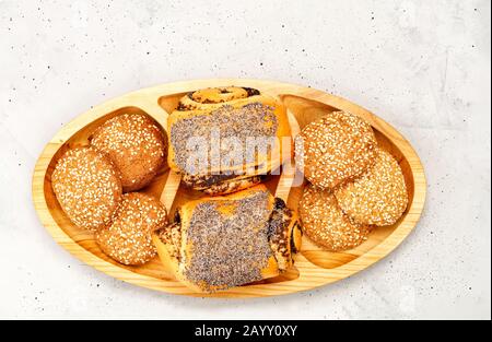 Frische Brötchen mit Mohnsamen und Plätzchen mit Sesamsamen auf einer Holzoberfläche, auf einem Hintergrund aus grauem Beton, Nahaufnahme, Kopierraum. Stockfoto