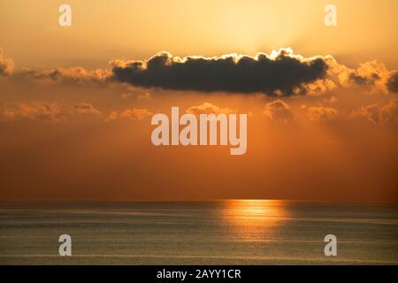 Dunkle Wolken blockieren die untergehende Sonne am orangefarbenen Abendhimmel über dem Mittelmeer Stockfoto