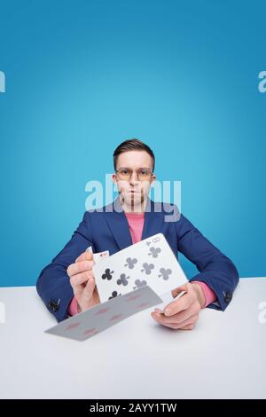Portrait eines ernsthaften intelligenten jungen bärtigen Kartenspielers in einer Brille, die am Tisch sitzt und Karten zur Kamera wirft Stockfoto