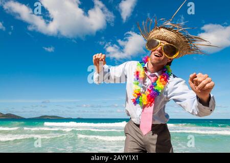 Büroangestellte im Urlaub, die Sonnenbrille, TouristenStrohhut und Lei tragen, die an einem tropischen Strand tanzen Stockfoto