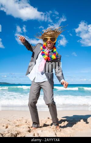 Fröhlicher Büroangestellter mit Sonnenbrille, Strohhut und Lei, der seinen Urlaub an einem tropischen Strand feiert Stockfoto