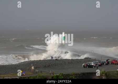 Stürmisches Wetter erzeugt große Wellen, die in Aberystwyth, Wales schwelgen, während Zuschauer von der Größe der Wellen in den Schatten gestellt werden. Stockfoto