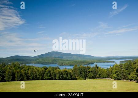 Float Plane Flying Over Moosehead Lake, Lodge at Moosehead Lake Lawn in Foreground, Greenvile, Maine. Stockfoto