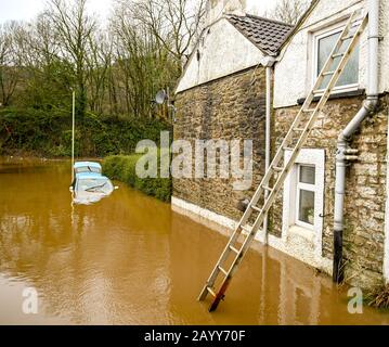 NANTGARW, IN DER NÄHE VON CARDIFF, WALES - FEBRUAR 2020: Leiter gegen Haus und ein Auto, das in Flutwasser auf einer Straße untergetaucht ist, nachdem der Fluss Taff seine Ufer platzte Stockfoto