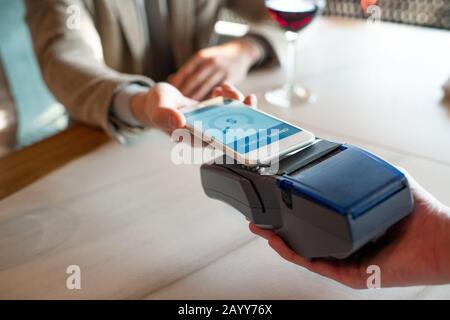 Horizontaler Nahaufnahme mit hohem Winkel von nicht erkennbarem Mann, der mit NFC auf dem Smartphone für das Essen im Restaurant bezahlt Stockfoto