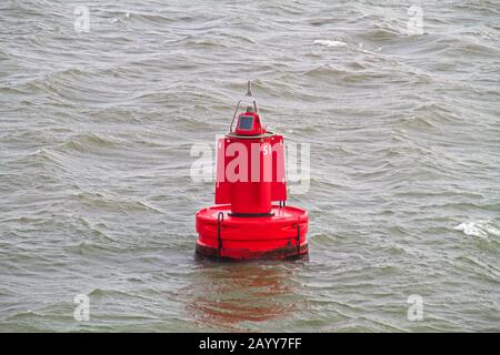 Auf der grauen Wasseroberfläche im niederländischen Wattenmeer schwimmt eine rote Boje Stockfoto