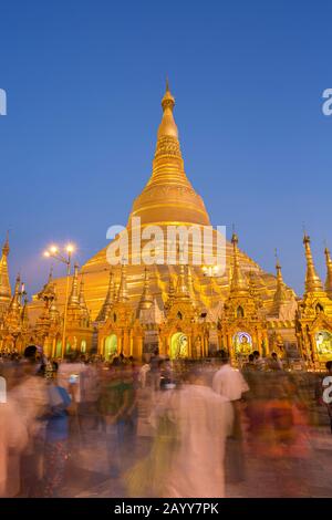 Viele Menschen vor der vergoldeten und beleuchteten Shwedagon-Pagode in Yangon, Myanmar, in der Abenddämmerung. Stockfoto