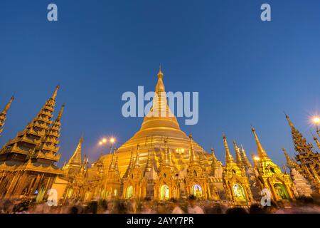 Viele Menschen vor der vergoldeten und beleuchteten Shwedagon-Pagode in Yangon, Myanmar, in der Abenddämmerung. Kopierbereich. Stockfoto