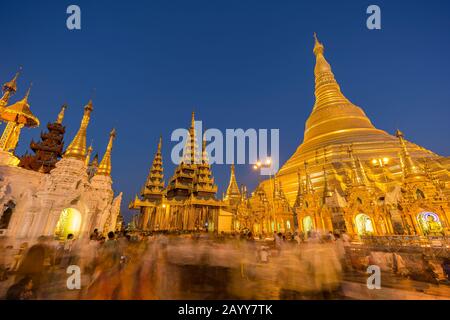 Viele Menschen vor der vergoldeten und beleuchteten Shwedagon-Pagode in Yangon, Myanmar, in der Abenddämmerung. Stockfoto